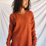 Front view of model wearing the Above All Else Sweater, which features rust-colored knit fabric with a front chest pocket, a round neckline, long sleeves, and side slits.