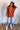 Full body front view of model wearing the Above All Else Sweater, which features rust-colored knit fabric with a front chest pocket, a round neckline, long sleeves, and side slits.