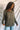 Front view of model wearing the Lost Without You Sweater, which features olive open-knit fabric with larger knitting on the sides, a round neckline, long sleeves, and a slouchy fit. Sweater is styled untucked.