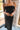 Close-up front view of model wearing the Magic Moment Dress in Black, which features black satin fabric with a midi-length hem, black feathers across the neckline, adjustable thin straps, and a back zipper