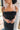 Close-up front upper view of model wearing the Magic Moment Dress in Black, which features black satin fabric with a midi-length hem, black feathers across the neckline, adjustable thin straps, and a back zipper