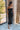 Front view of model wearing the Magic Moment Dress in Black, which features black satin fabric with a midi-length hem, black feathers across the neckline, adjustable thin straps, and a back zipper