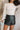 Front view of model wearing the Talk That Talk Skort, which features black faux-leather with silver studs, a front skirt overlay, and a back zipper.