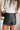 Close-up front view of model wearing the Talk That Talk Skort, which features black faux-leather with silver studs, a front skirt overlay, and a back zipper.