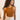 Front view of model wearing the Risk It Bodysuit in Camel, that has stretchy double-layered fabric, a high round neckline, thick straps, and a thong bottom with snap closures. Worn under cream pants