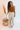 Full body front view of model wearing the Risk It Bodysuit in Camel, that has stretchy double-layered fabric, a high round neckline, thick straps, and a thong bottom with snap closures. Worn under cream pants