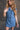 Front view of model wearing the Regina Blue Denim Sleeveless Dress which features blue denim fabric, button up, two front buttoned chest pockets, collared neckline and sleeveless.