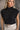 Front view of model wearing the Lola Black Sleeveless Turtleneck Sweater which features black cable knit fabric, a thick hem, a cropped waist, a turtleneck neckline, and a sleeveless design.