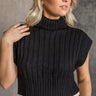 Front view of model wearing the Lola Black Sleeveless Turtleneck Sweater which features black cable knit fabric, a thick hem, a cropped waist, a turtleneck neckline, and a sleeveless design.