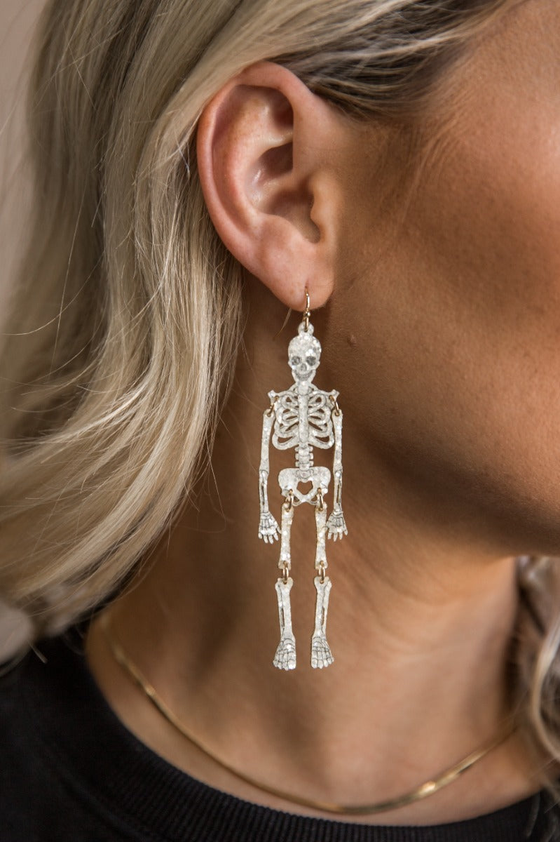 Side view of model wearing the Sally White Glitter Skeleton Earrings that feature white glitter skeleton shaped dangle earrings with gold link details.