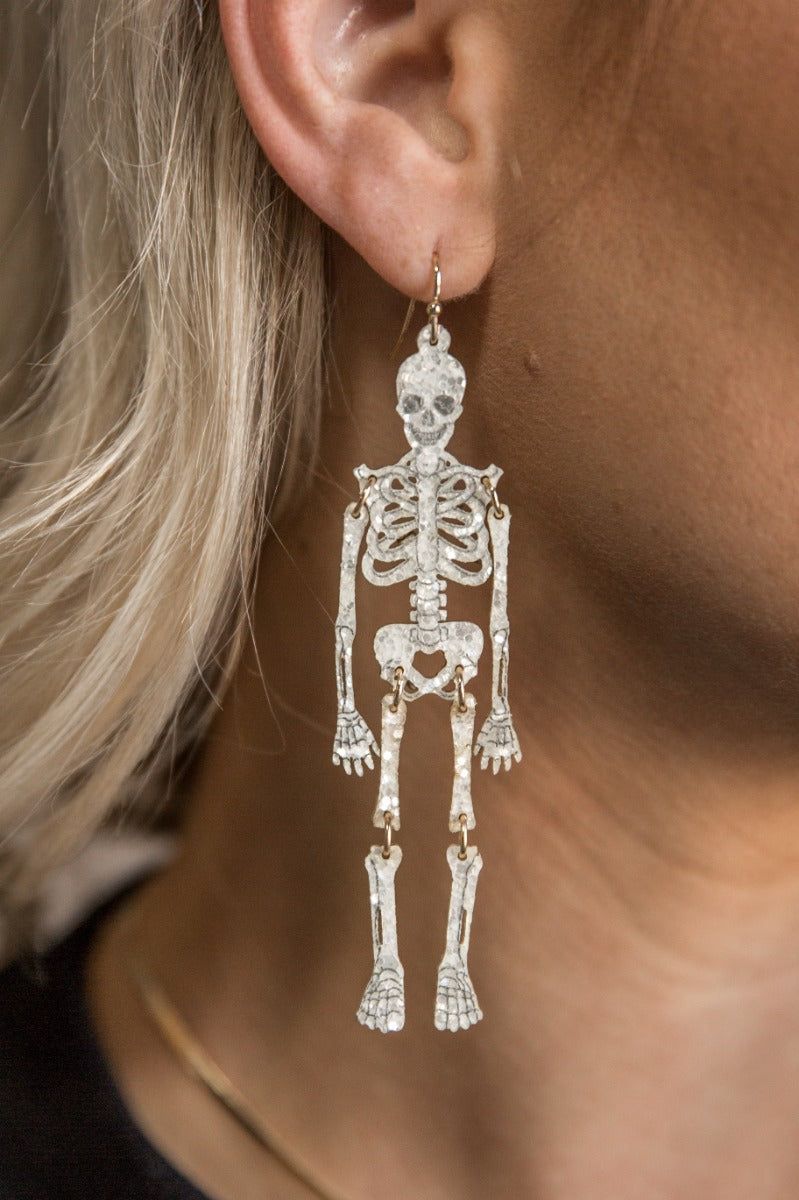 Side view of model wearing the Sally White Glitter Skeleton Earrings that feature white glitter skeleton shaped dangle earrings with gold link details.