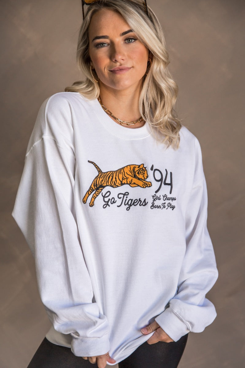 Front view of model wearing the Girl Champs Tiger Long Sleeve Sweatshirt which features white knit fabric, thick hem, round neckline, black and gold stitch tiger that says "Go Tigers '94, Girl Champs Born To Play" and long sleeves with cuffs.