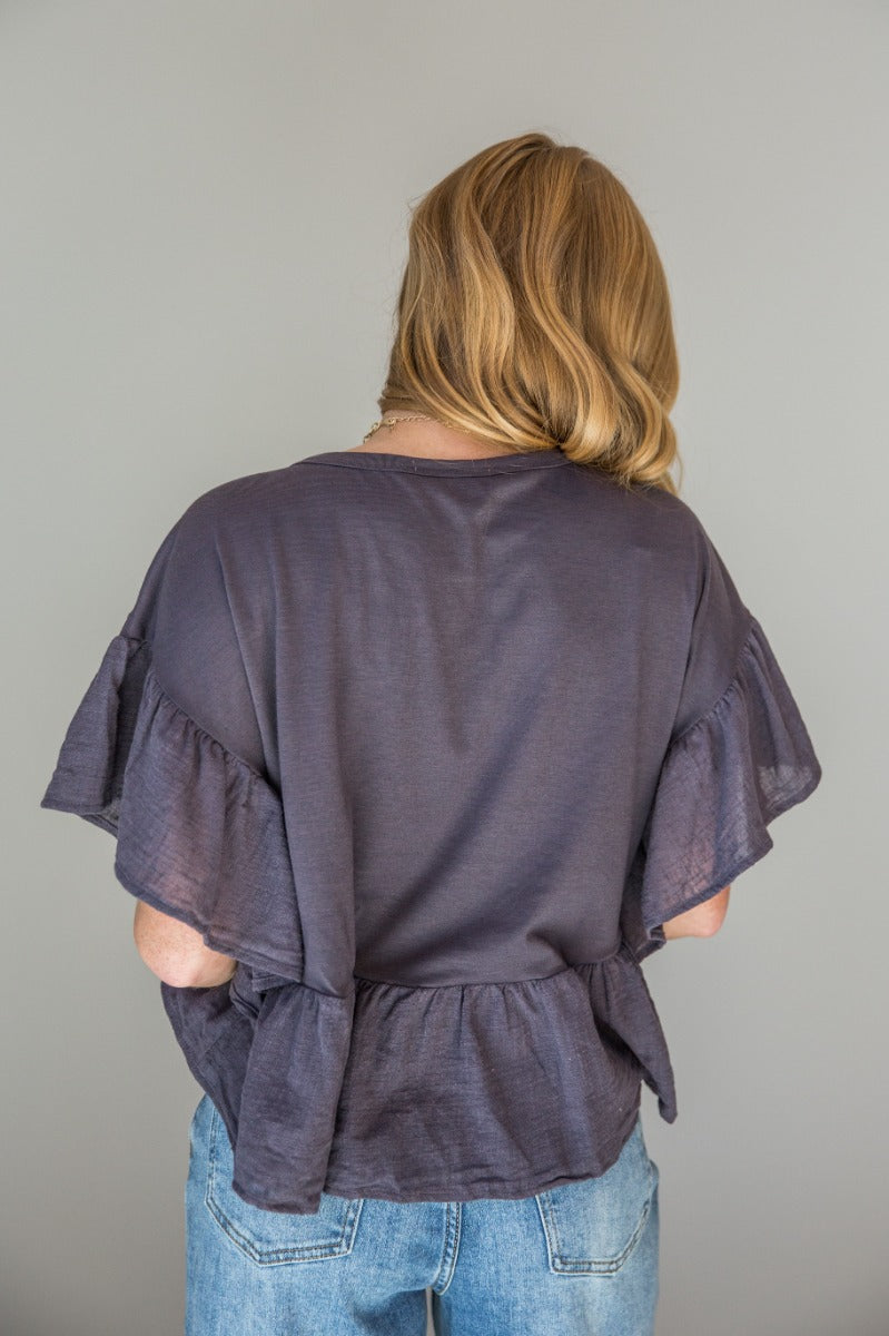 Back view of model wearing the Alyssa Charcoal Ruffled Short Sleeve Top that has charcoal knit fabric, ruffled guaze short sleeves, a gauze peplum bottom, and a notched neckline.