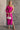 Full body front view of model wearing the Dahlia Pink One-Shoulder Ruched Midi Dress that has lightweight pink knit fabric, a one-shoulder neckline with 1 long sleeve, a back cutout, ruched sides, and a side slit.