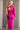 Full body back view of model wearing the Dahlia Pink One-Shoulder Ruched Midi Dress that has lightweight pink knit fabric, a one-shoulder neckline with 1 long sleeve, a back cutout, ruched sides, and a side slit.