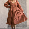 Full body front view of model wearing the Wrenley Rust Long Sleeve Midi Dress that has rust gauze fabric, a tiered body, long balloon sleeves with elastic, side pockets, a v neck, and a smocked back.