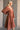 Side view of model wearing the Wrenley Rust Long Sleeve Midi Dress that has rust gauze fabric, a tiered body, long balloon sleeves with elastic, side pockets, a v neck, and a smocked back.