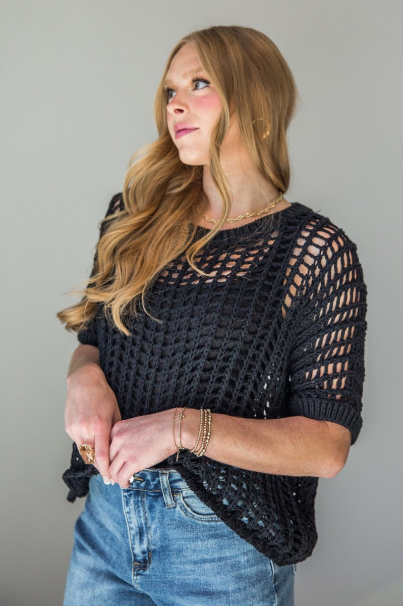 Front view of model wearing the Tatum Black Open Knit Short Sleeve Top which features black crochet knit fabric, round neckline and short sleeves.