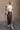 Full body view of model wearing the Angela Brown Front Slit Midi Skirt which features brown cotton fabric, midi length, front slit detail, front zipper with button closure, belt loops, two front pockets, two back pockets and fray hem.