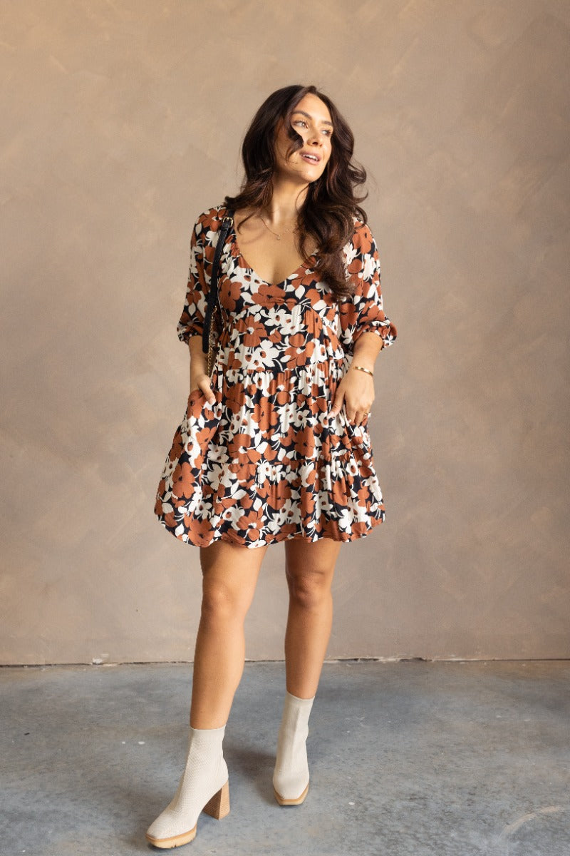Full body front view of model wearing the Selah Black & Brown Floral Mini Dress that has a black, brown and white floral print, a flare skirt,a scooped neckline, short puff sleeves, and a smocked back.