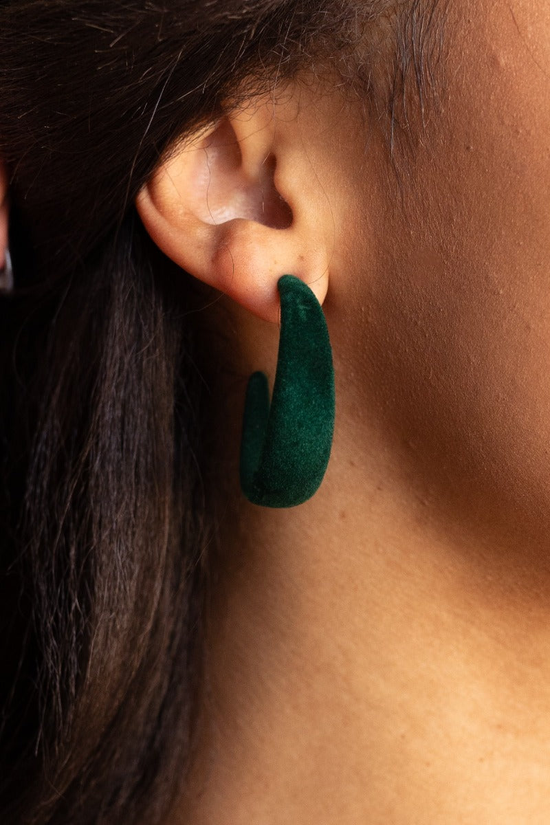 Close up view of model wearing the Sadie Green Velvet Hoop Earrings that feature medium open hoops with dark green velvet fabric.