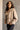 Frontal side view of model wearing the Nova Taupe Knit Quilt Jacket which features taupe cable knit fabric and taupe quilted fabric, two front slit pockets, brown tortoise buttons, a high neckline with a hood attached, and long puff sleeves with cuffs.