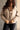 Front view of model wearing the Nova Taupe Knit Quilt Jacket which features taupe cable knit fabric and taupe quilted fabric, two front slit pockets, brown tortoise buttons, a high neckline with a hood attached, and long puff sleeves with cuffs.