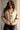 Front view of model wearing the Nova Taupe Knit Quilt Jacket which features taupe cable knit fabric and taupe quilted fabric, two front slit pockets, brown tortoise buttons, a high neckline with a hood attached, and long puff sleeves with cuffs.