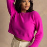 Front view of model wearing the Aria Fuchsia Long Sleeve Sweater which features fuchsia textured knit fabric, ribbed trim, a cropped waist, a round neckline, dropped shoulders, and long sleeves with ribbed trim.