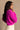 Side view of model wearing the Aria Fuchsia Long Sleeve Sweater which features fuchsia textured knit fabric, ribbed trim, a cropped waist, a round neckline, dropped shoulders, and long sleeves with ribbed trim.