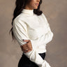 Side view of model wearing the Gabriela Cream Turtleneck Sweater which features cream knit fabric, ribbed trim, a turtleneck neckline, dropped shoulders, and long sleeves with cuffs.