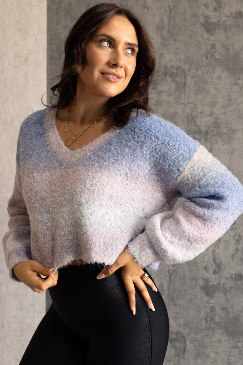 Front view of model wearing the Emery Blue Multi Textured Long Sleeve Sweater which  features blue, light blue, grey, purple and light pink popcorn knit fabric, ombre stripe design, cropped waist, round neckline and long puff sleeves with cuffs.