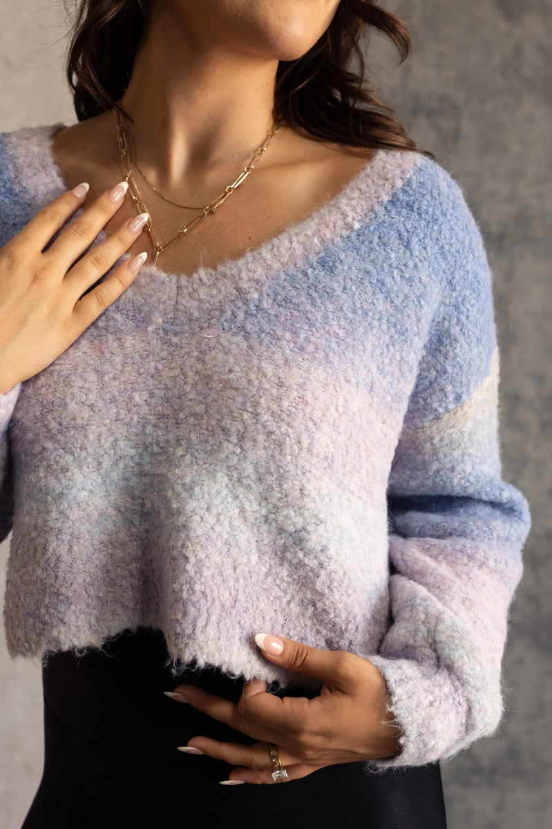 Close up view of model wearing the Emery Blue Multi Textured Long Sleeve Sweater which  features blue, light blue, grey, purple and light pink popcorn knit fabric, ombre stripe design, cropped waist, round neckline and long puff sleeves with cuffs.