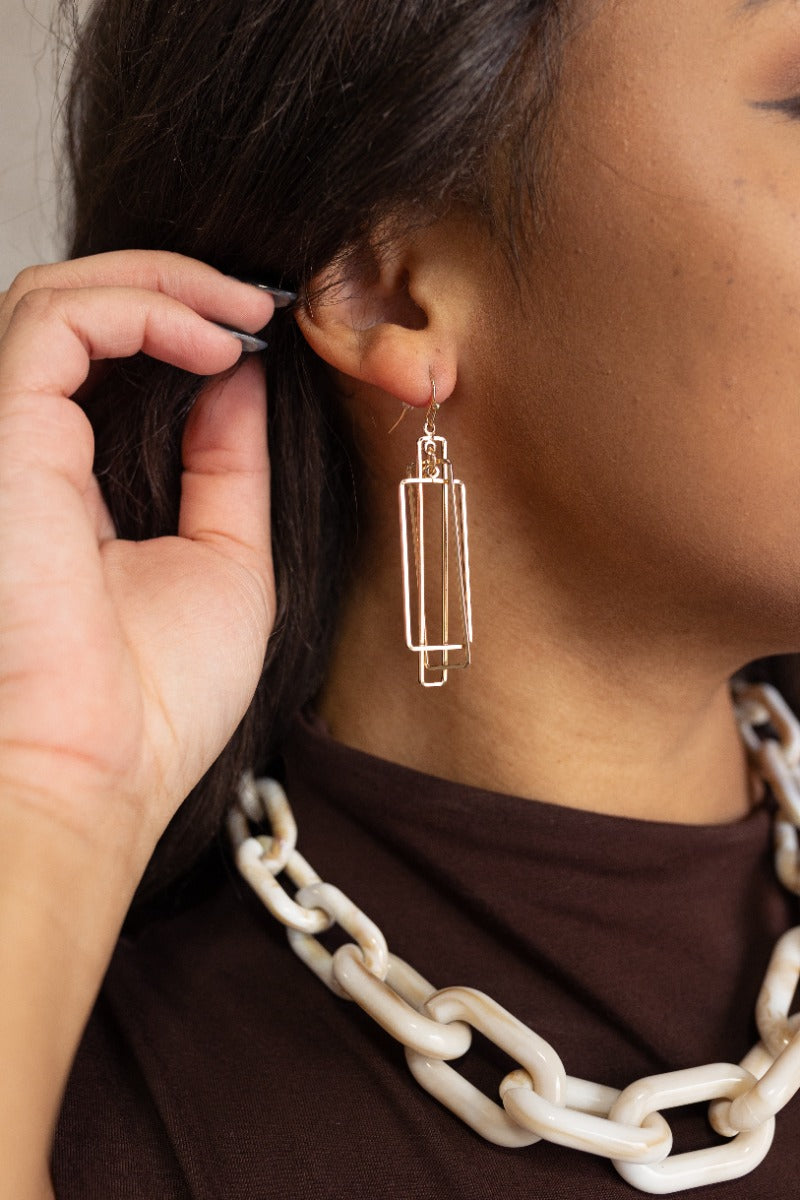 Side image of model wearing the Delilah Gold Geometric Earrings that feature layered gold rectangle pendants and a hook back.