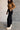 Full body side view of model wearing the Aubrey Black Lounge Pants which features black cotton fabric, two front pockets, an elastic waistband with drawstring ties, and wide legs.