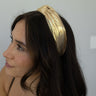 Side view of model wearing the Gabriella Gold Metallic Headband that features gold metallic fabric, black lining, and a knot design.