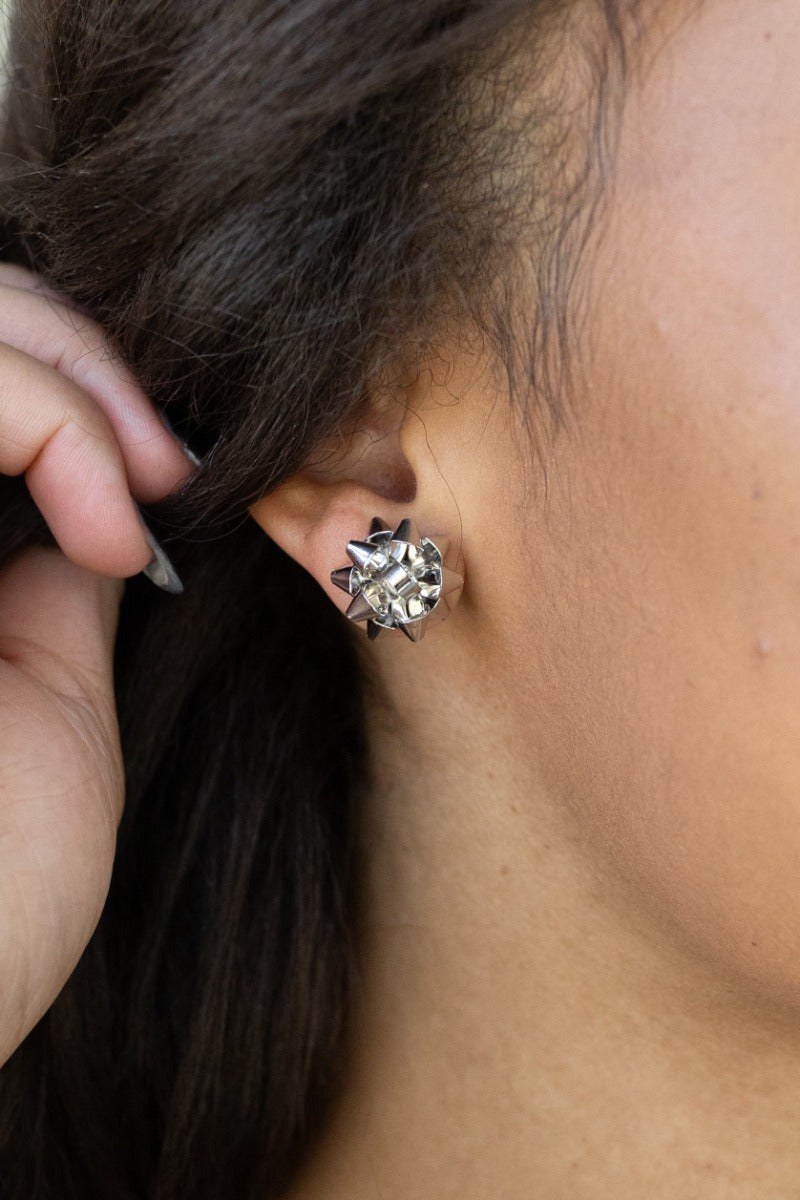 Clsoe-up view of model wearing the Bella Silver Bow Stud Earrings that feature silver studs shaped as a present bow.