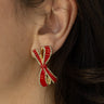 Close-up side view of model wearing the Noel Red Bow Earrings that feature red bow-shaped studs with red, light green and clear rhinestones and set in gold.
