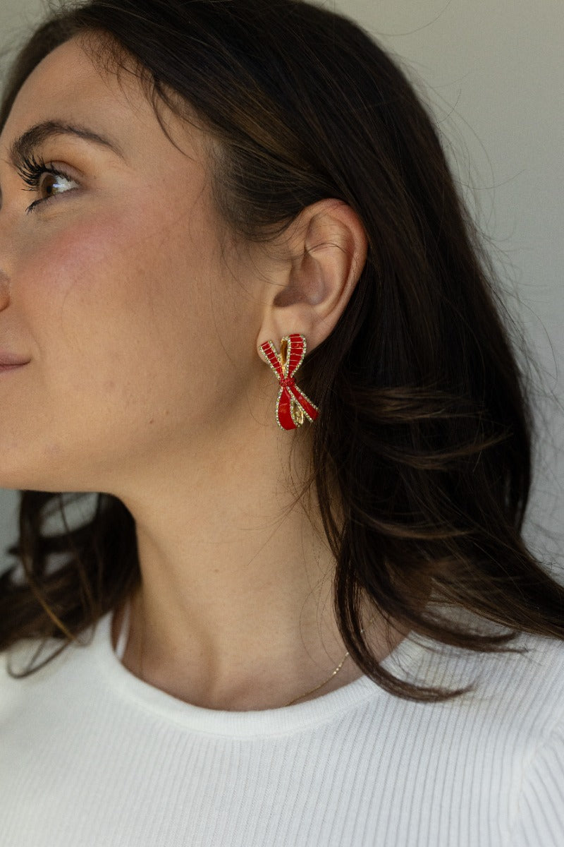 Side view of model wearing the Noel Red Bow Earrings that feature red bow-shaped studs with red, light green and clear rhinestones and set in gold.