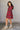 Full body side view of model wearing the Victoria Red Multi Plaid Tiered Mini Dress which features red cotton fabric with a dark blue, light blue, green and white plaid pattern, mini length, two-tiered body style, a round neckline with a v cut-out, a tie 