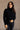 Front view of model wearing the Gabriela Black Turtleneck Sweater that has black knit fabric, ribbed trim, a turtleneck neckline, dropped shoulders, and long sleeves with cuffs.