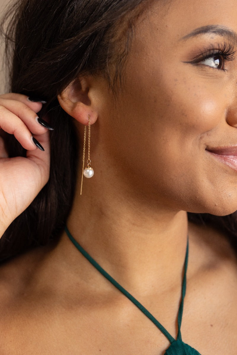 Side view of model wearing the Leilani Pearl Threader Earrings that feature gold chains linked to faux pearl beads.