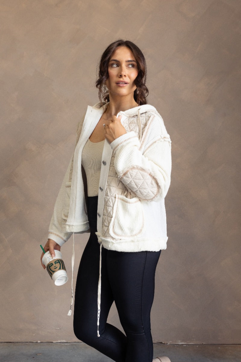 Side view of model wearing the Everlee Cream Mixed Fabric Hooded Shacket that hascream textured fabric, white waffle knit fabric, beige quilted fabric, brown stitching, pockets, a hood and long sleeves.