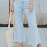 Front view of model wearing the Aubrey Cropped Flare Jeans that have light blue denim, a front zipper with button closure, two back pockets, and cropped flare legs with raw hems