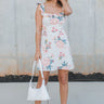 Full body front view of model wearing the In Full Bloom Dress that has ivory fabric with a pink, red, yellow and teal floral pattern, a scoop neckline with ruffle details, ruffle straps, and a smocked cut-out back.