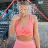 Front view of model wearing the Live Your Best Life Crop Top that has coral pink ribbed fabric, a cropped waist, a criss cross body, a deep v neckline, thick straps, and a sleeveless design.