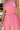 Close-up front view of model wearing the Wild At Heart Jumpsuit that has pink satin fabric, an elastic waist, a square neck, spaghetti straps, an open back with corset ties, and flare legs