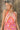 Close front view of model wearing the Trip To The Tropics Maxi Dress that has orange, fuchsia, purple, pink and ivory fabric with a floral pattern,  two tiered body, a halter neck, a cinched waist, and an open back.