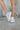 Front and side view of model wearing the Aria Sneakers which features champagne, grey and white color tones, suede upper, cream laces, grey glitter and grey star design and platform sole. 