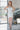Full body front view of model wearing the All Eyes On Me Dress that has white sheen fabric, white lining, mini length, an overlapped hem, one shoulder strap, and a monochromatic back zipper.